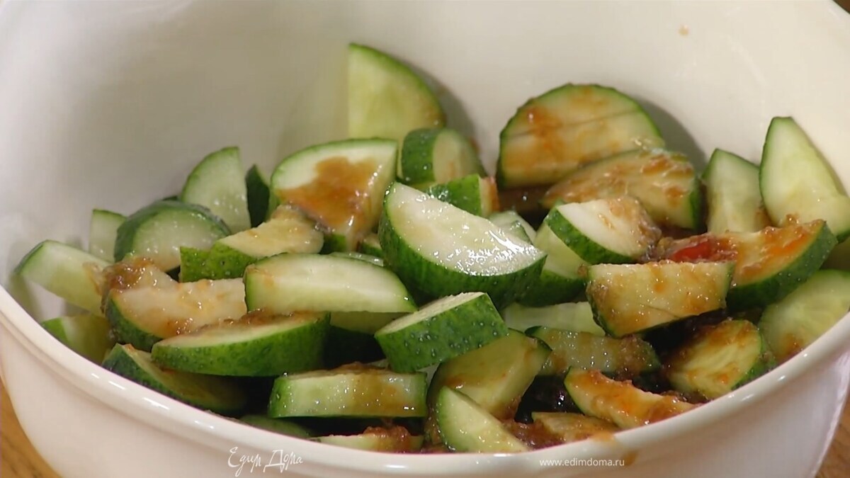 Огурцы нарезать полукружьями, выложить в глубокую миску и полить заправкой.