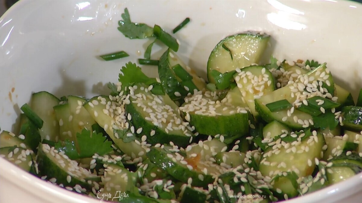 К огурцам добавить измельченную зелень, все перемешать и посыпать кунжутом.