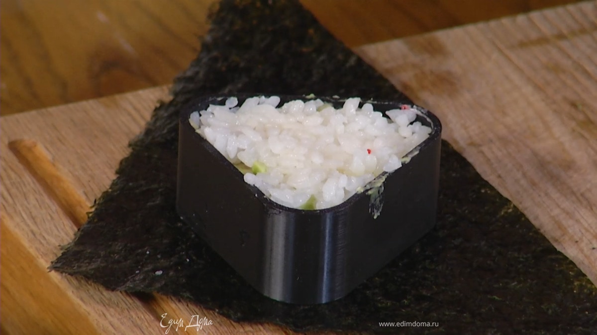 Помещая треугольную формочку в центр каждого листа нори, уложить в нее немного риса и слегка утрамбовать, затем выложить семгу, авокадо и сверху еще немного риса.