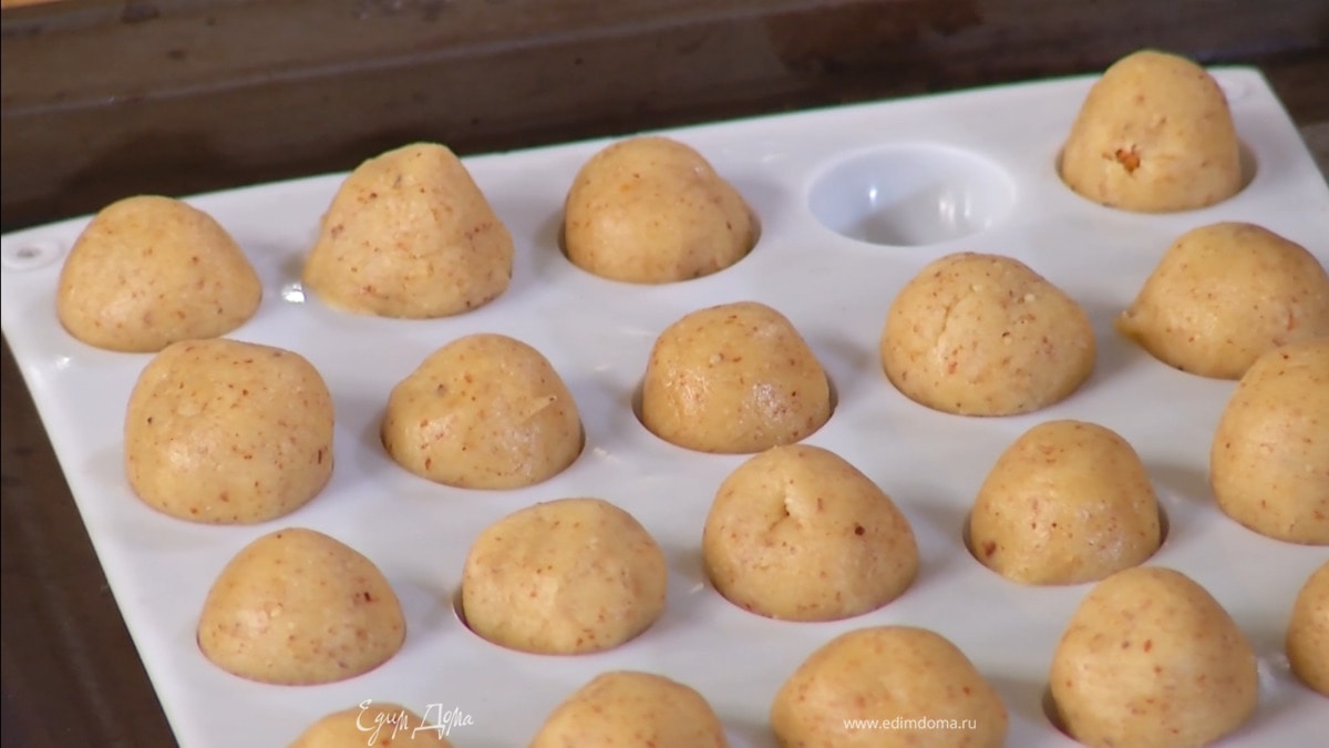 Скатать из теста маленькие шарики, в центр некоторых воткнуть миндальный орех и поместить в форму для печенья с маленькими круглыми выемками.