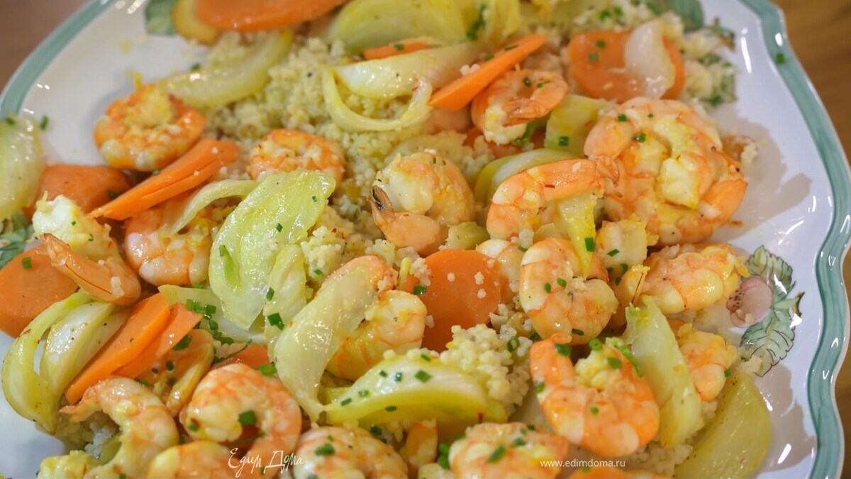Готовый кускус разрыхлить вилкой, влить оливковое масло Extra Virgin, перемешать и выложить на тарелку, сверху разложить креветки с овощами, посыпать оставшимся шнитт-луком.