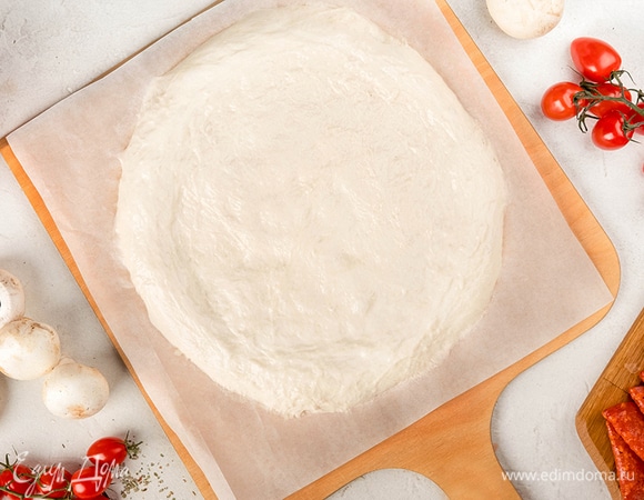 Выложите готовое тесто на пергамент и разгладьте его до нужного диаметра. Сформируйте небольшие бортики. Отправьте в разогретую духовку на 3–4 минуты.