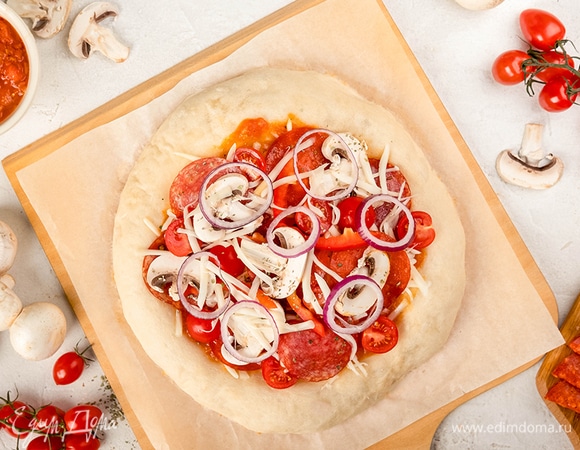 Достаньте тесто, нанесите на него соус, кружочки колбасы, половинки черри, грибы и моцареллу. 