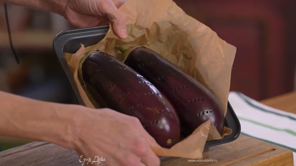 Баклажаны выложить в небольшую форму, выстеленную бумагой для выпечки, часто наколоть вилкой и запекать в разогретой духовке, так чтобы кожица слегка обгорела.