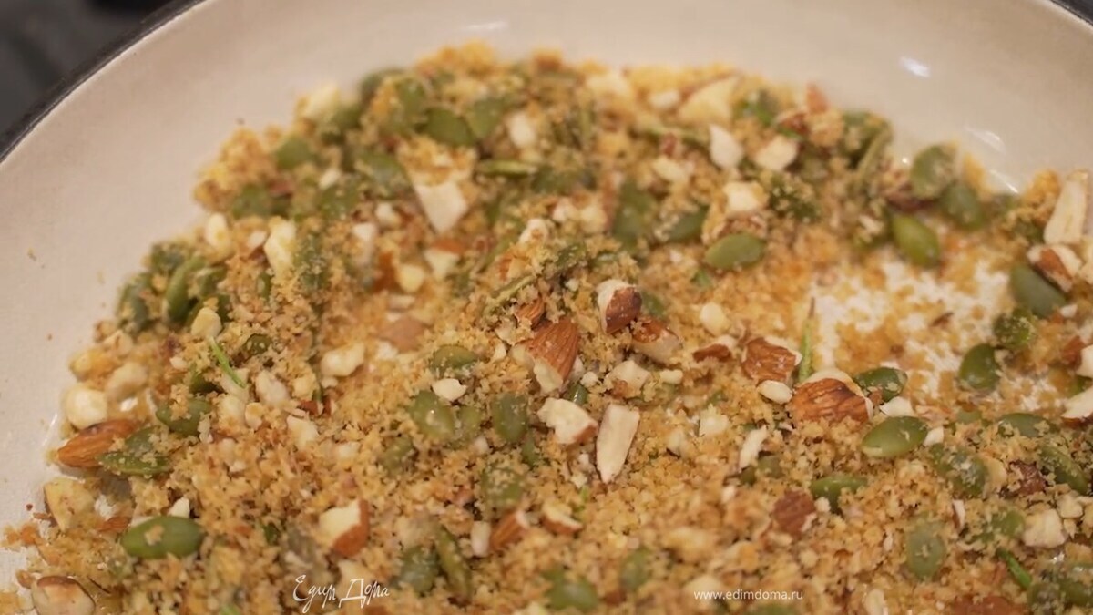 В отдельную сковороду влить оставшееся оливковое масло, выложить тыквенные семечки, измельченный миндаль, раскрошить острый перец, посолить, добавить листья розмарина, панировочные сухари и подсушить все на небольшом огне.