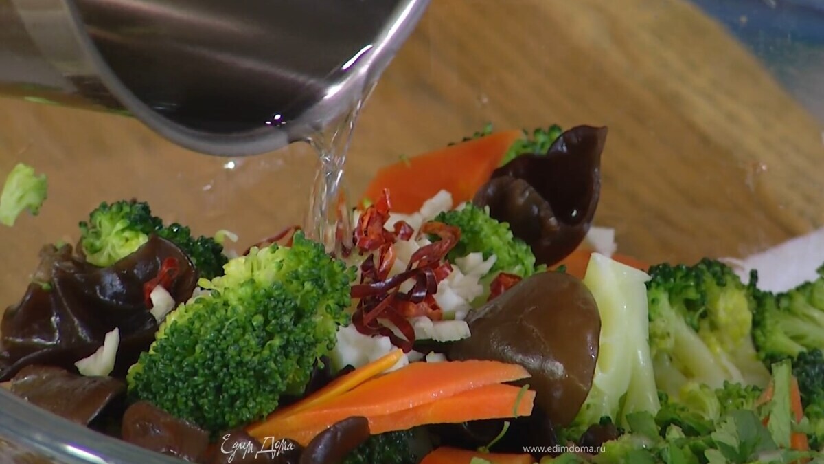 Кинзу мелко порезать и добавить в миску с овощами, рядом выложить чеснок и перец чили и полить их разогретым растительным маслом, затем влить соевый соус, кунжутное масло и рисовый уксус, все перемешать и посыпать кунжутом.