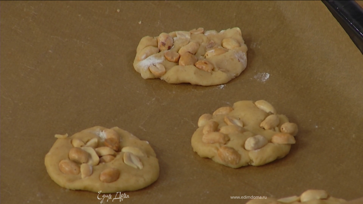 Из охлажденного теста сформировать небольшие тонкие лепешки и выложить их на рабочую поверхность, присыпанную оставшейся мукой. На каждое печенье выложить как можно больше арахиса и переложить на противень, выстеленный бумагой для выпечки.