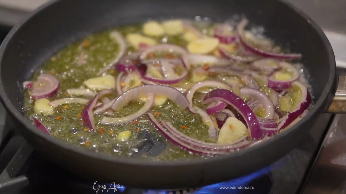 В тяжелой сковороде разогреть растительное и сливочное масло, выложить лук и чеснок, посолить, посыпать хлопьями чили и обжарить.