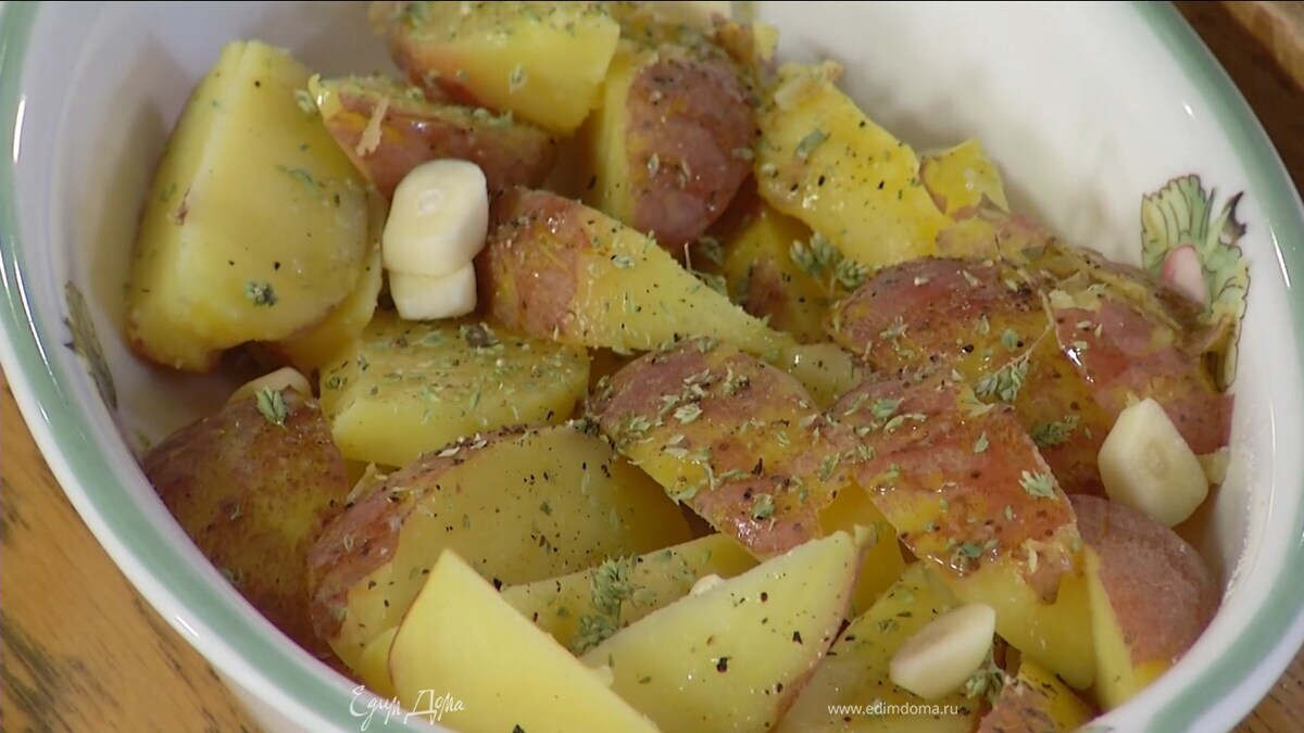 Выложить нарезанный картофель в жаропрочную форму, слегка сбрызнуть оливковым маслом, посолить, поперчить, сверху разложить чеснок и посыпать орегано.