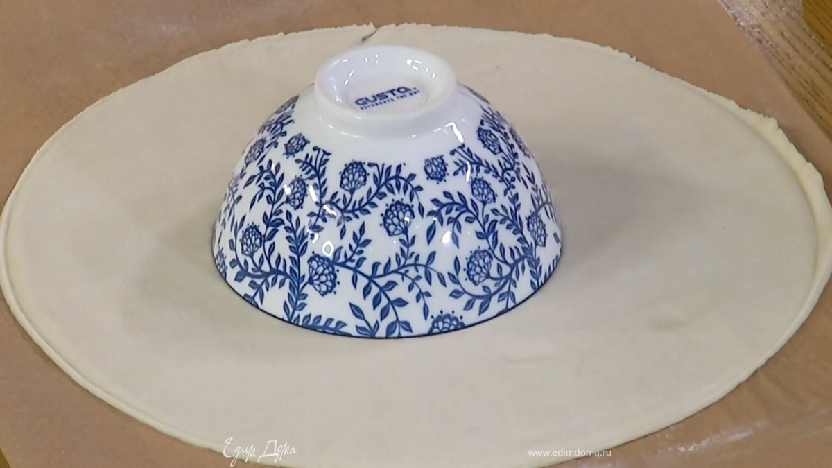 Тесто предварительно разморозить и на бумаге для выпечки раскатать в тонкий пласт, затем вместе с бумагой переложить на противень и вырезать из теста круг, в центр поместить перевернутую пиалу.