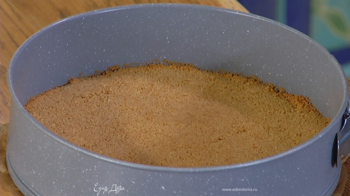 Дно разъемной формы выстелить бумагой для выпечки, выложить песочную крошку и утрамбовать в корж, затем отправить в разогретую духовку на 8–10 минут.