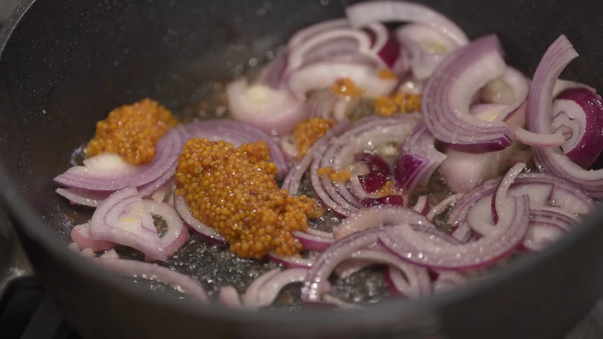 Красный лук почистить, нарезать полукольцами и выложить в сотейник, где жарилось мясо, добавить немного соли, горчицу, кленовый сироп, все перемешать и обжарить.