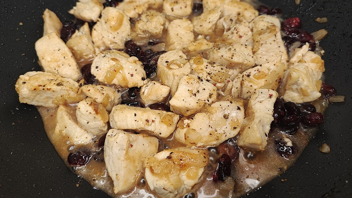 Убавьте огонь до среднего. Посолите мясо, добавьте перец, кориандр, сушеную клюкву. Влейте апельсиновый сок и потомите под крышкой еще 5 минут, чтобы ягоды немного набухли, а мясо напиталось ароматом. Можно использовать не готовый сок, а выжать его с половинки апельсина. В этом случае не будет лишним добавить в сковороду немного цедры, добытой с помощью мелкой терки.